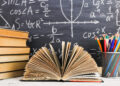 School desk in the classroom, with books on background of chalk board with written formulas. Soncept Teacher's Day.
